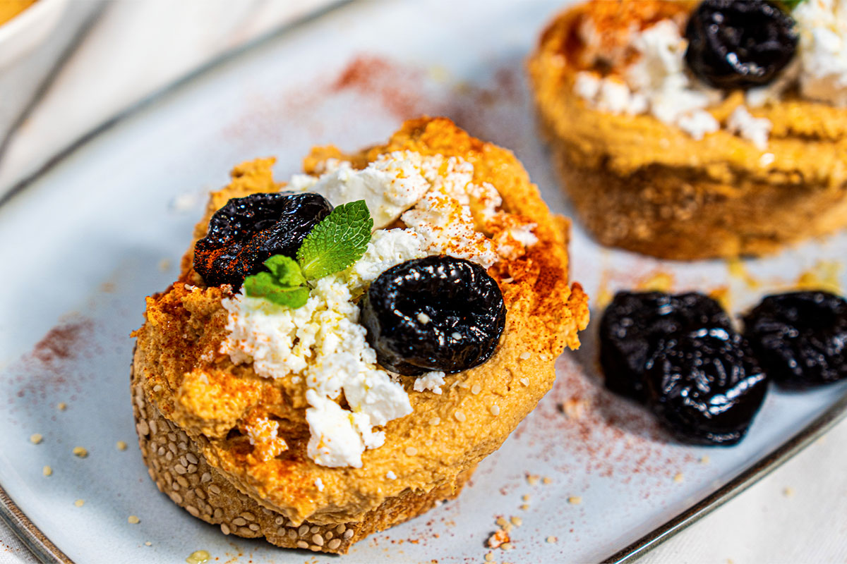 Crostini di pane con hummus, feta, prugne della California, menta e paprika Crostini di pane con hummus, feta, prugne della California, menta e paprika